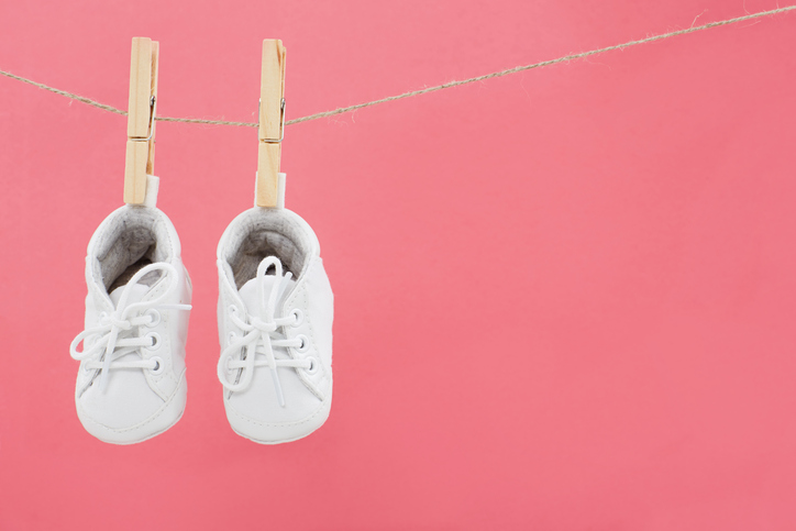 Baby shoes hanging on washing line against pink